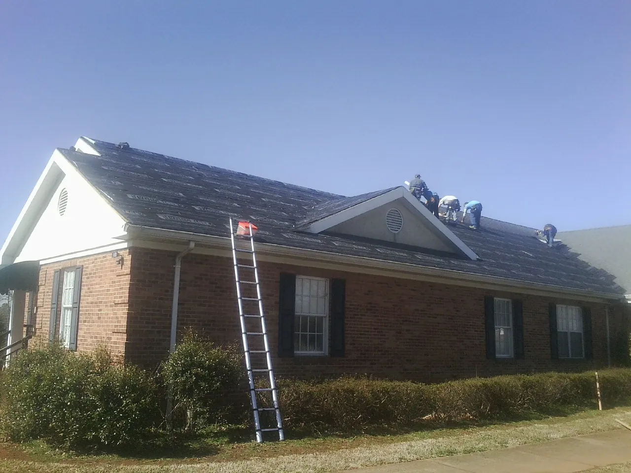 Crew tearing shingles off a brick ranch roof with a ladder set — Emergency Roof Repair work by our crew in Kiamesha Lake