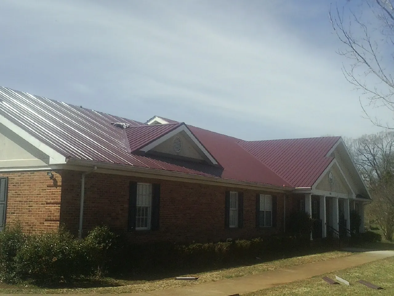 Red metal roof with gabled entries on a long brick building, from a Hail Damage Roof Repair job in Kiamesha Lake