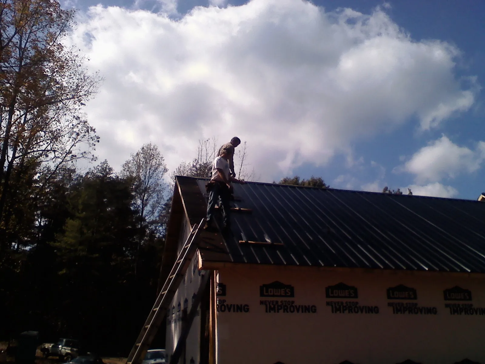 Roofer fastening dark metal panels high against a cloudy sky, from a Roof Inspection job in Kiamesha Lake