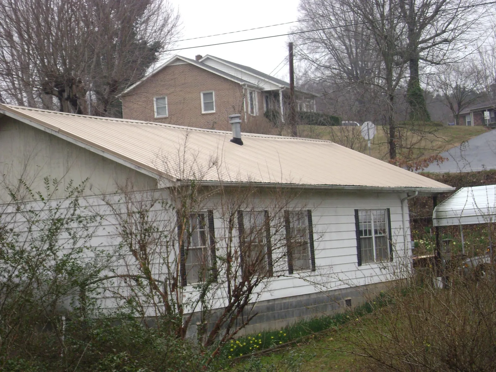 Tan metal roof on a white sided house set into a hillside — Commercial Roofing by Roofing Brothers in Kiamesha Lake